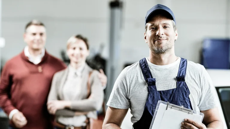 Technician in overalls holding a clipboard, with two customers standing behind him
