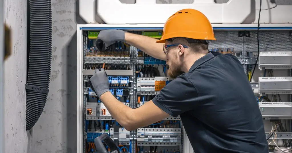 Electrician in a hard hat working inside a breaker panel