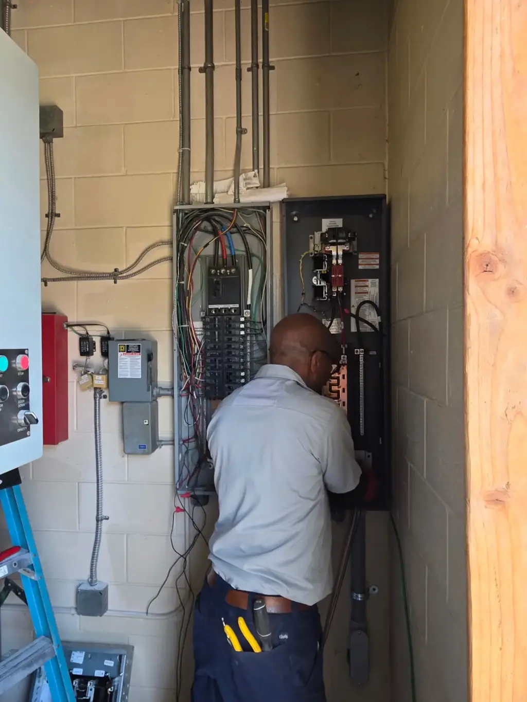 Electrician working on breaker panels mounted on a block wall
